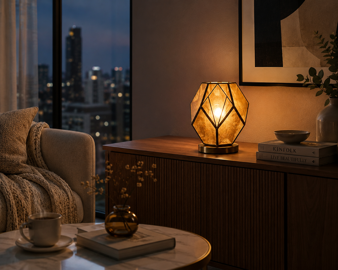 Elegant geometric table lamp glowing warmly on a wooden sideboard in a cozy modern living room, with a city view in the background.